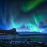 green aurora lights over rocky shore during night time